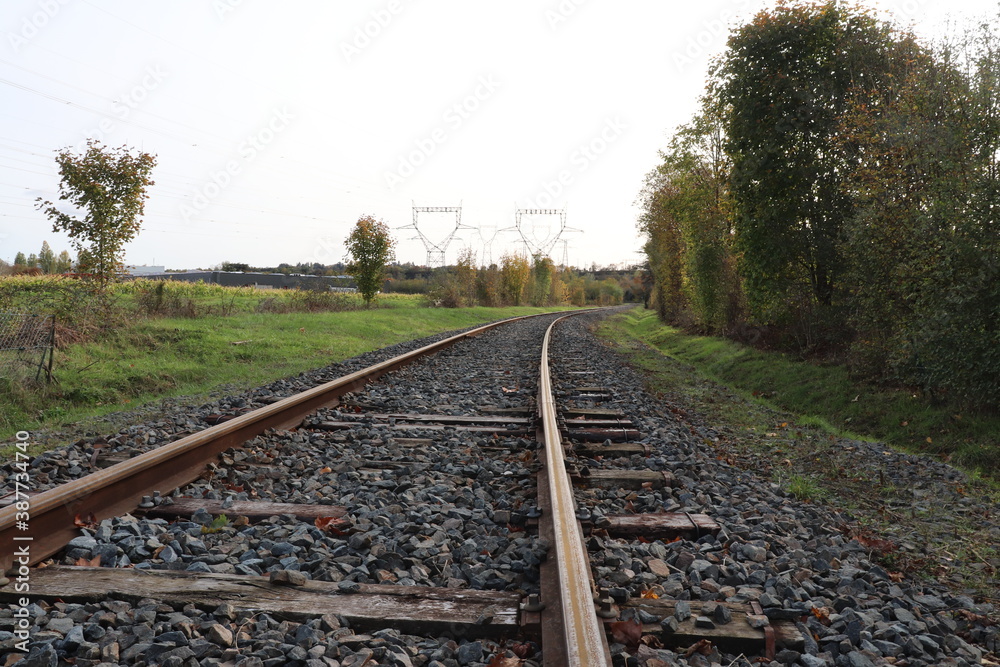 Fototapeta premium Voie de chemin de fer unique avec traverses en bois de type vignole, au milieu de la campagne en automne, ville de Saint Quentin Fallavier, département de l'Isère, France