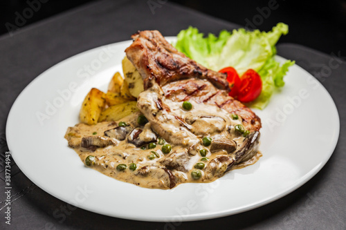 Grilled pork meat on the bone with mushroom sauce, green peas, potato and cherry tomato