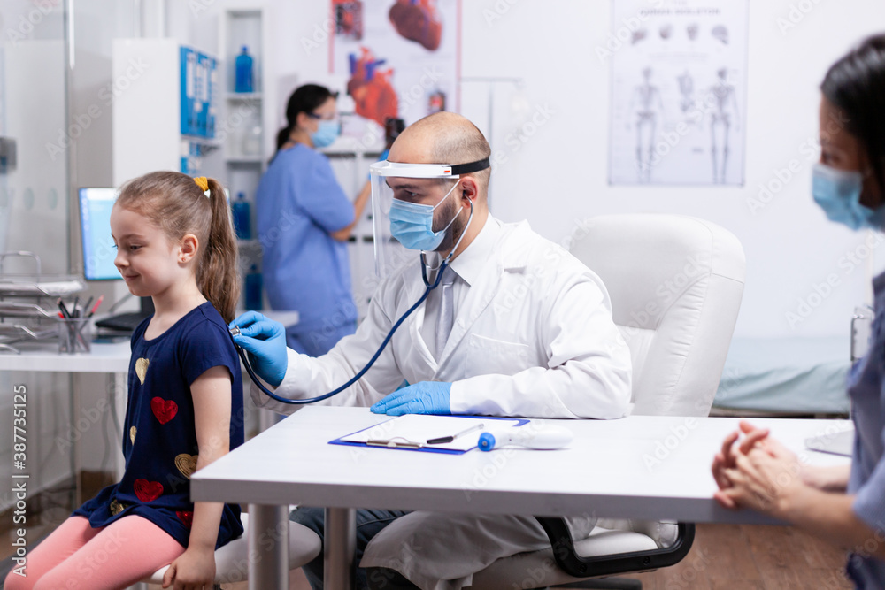 Obraz premium Doctor using stethoscope during examination on little girl. Health pediatrician specialist providing health care services consultations treatment in protective equipment for consultation