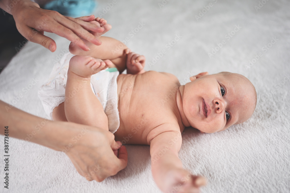 Mother is changing diaper for cute emotional funny newborn little infant baby boy laying in crib Mother is changing diaper for cute emotional funny newborn little infant baby boy laying in crib