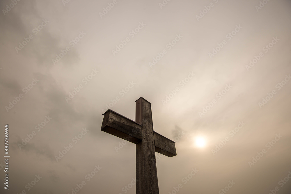 Simple oak wood catholic cross, sun shining behind thick rain clouds.