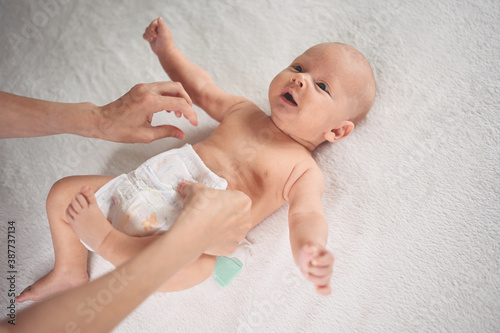 Mother is changing diaper for cute emotional funny newborn little infant baby boy laying in crib