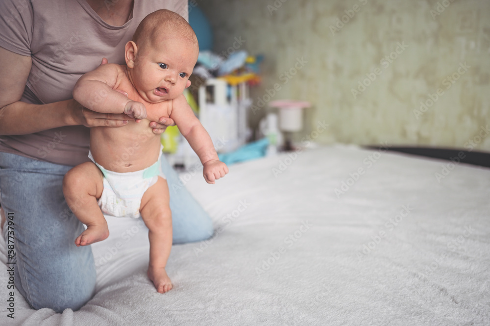 Mom doing exercises for baby in diaper. Cute emotional funny newborn boy learns to walk. Mom doing exercises for baby in diaper. Cute emotional funny newborn boy learns to walk.