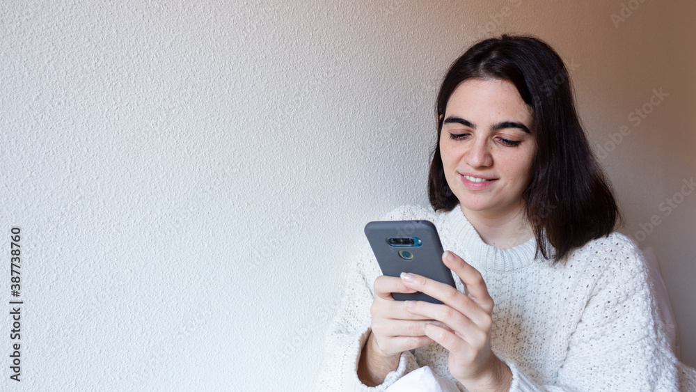 Woman indoor portrait. Young beautiful using her mobile phone. woman in warm knitted clothes at home. fashion. Autumn, winter Woman indoor portrait. Young beautiful using her mobile phone. woman in warm knitted clothes at home. fashion. Autumn, winter