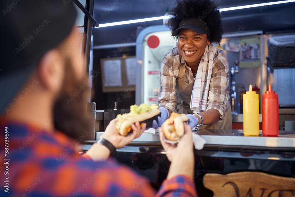 polite afro-american female employee holding, giving, two sandwiches to a  beardy caucasian customer. fast food service Stock Photo | Adobe Stock