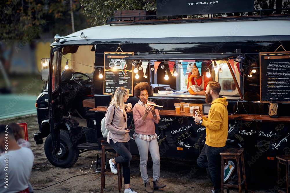 friends eating, drinking, talking, socializing outdoor in front of modifed truck for fast food service - obrazy, fototapety, plakaty 