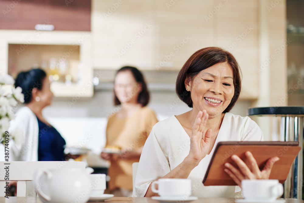Smiling senior woman with digital tablet sitting at kitchen table and video calling her relative Smiling senior woman with digital tablet sitting at kitchen table and video calling her relative