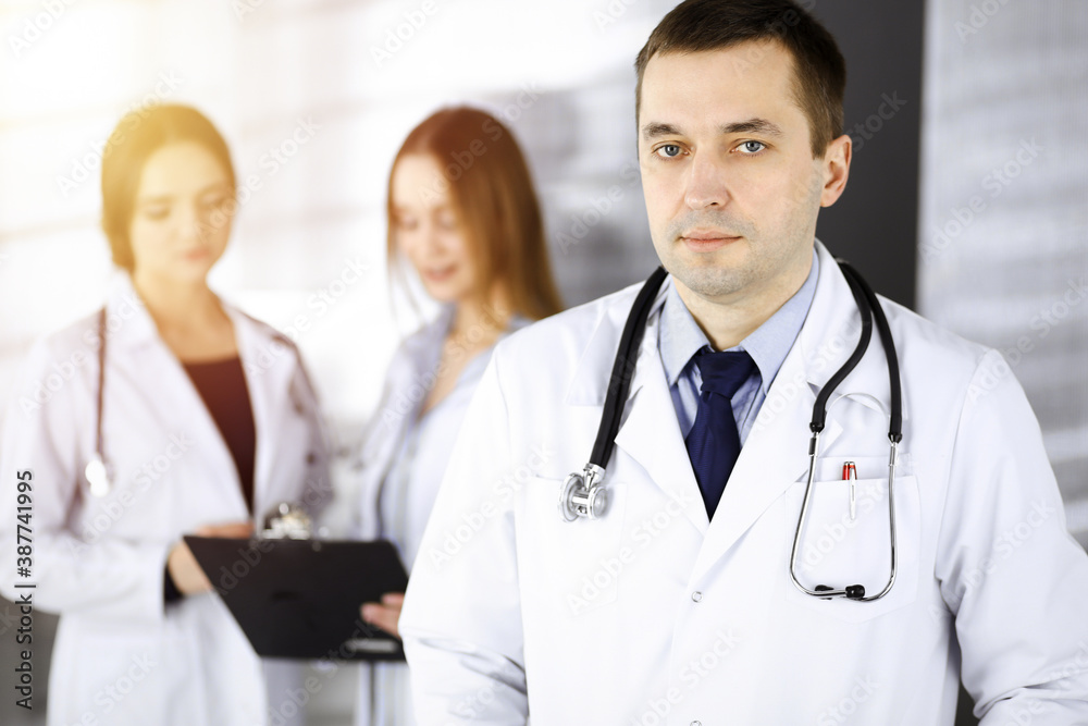 Professional middle aged doctor with a stethoscope at work with colleagues in a sunny clinic. Perfect medical service in a hospital. Medicine and healthcare concept Professional middle aged doctor with a stethoscope at work with colleagues in a sunny clinic. Perfect medical service in a hospital. Medicine and healthcare concept