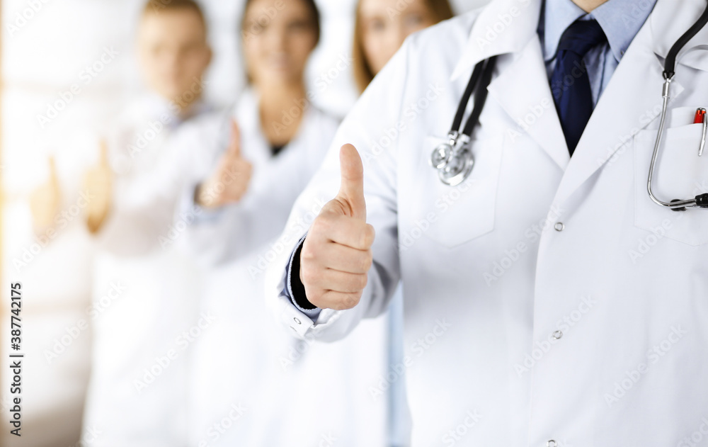 Group of professional doctors are standing as a team with thumbs up in a sunny hospital office, ready to help their patients. Medical help, insurance in health care and medicine concept Group of professional doctors are standing as a team with thumbs up in a sunny hospital office, ready to help their patients. Medical help, insurance in health care and medicine concept