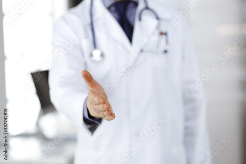 Unknown male doctor standing straight and offering helping hand in clinic near his working place, closeup. Perfect medical service in hospital. Medicine and healthcare concept