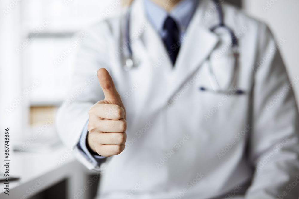 Unknown male doctor sitting with thumbs up sign at his working place in clinic, closeup. Perfect medical service in hospital. Medicine and healthcare concept Unknown male doctor sitting with thumbs up sign at his working place in clinic, closeup. Perfect medical service in hospital. Medicine and healthcare concept