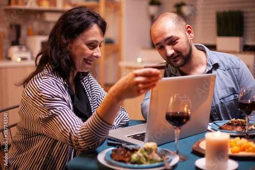 Woman holding credit card while doing shopping with husband during dinner. Adults sitting at the table  searching  browsing  surfing  using technology card payment  internet