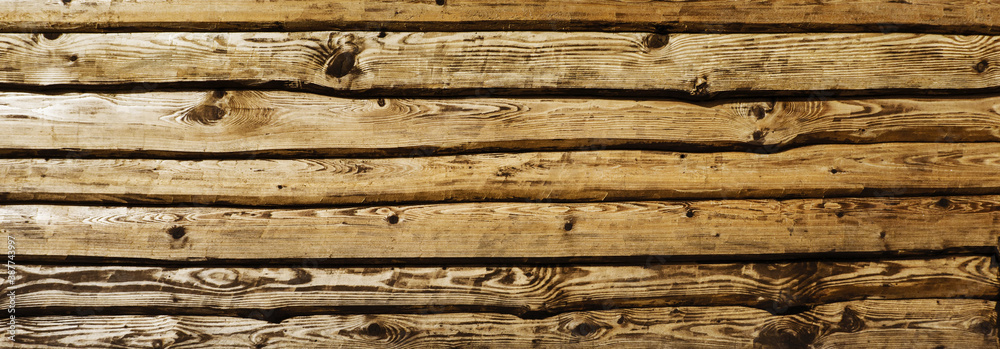 Fototapeta premium Raw wood texture. Brown wooden wall background. Rustic desks with knots pattern. Countryside architecture wall. Village building construction. Horizontal panoramic background for website header.