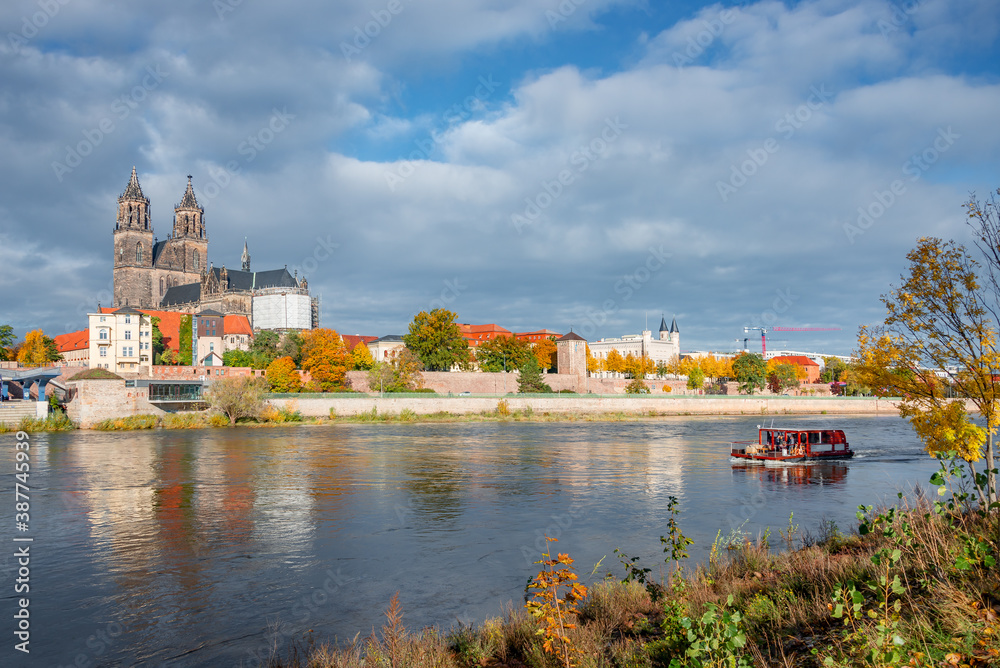 Obraz premium Historical and shopping downtown of Magdeburg, old town, Elbe river and magnificent Cathedral at early Autumn, with a party boat passing by, Germany, at sunny day but heavy clouds.