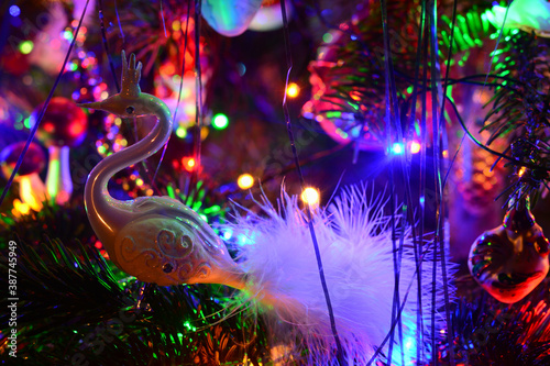 Christmas tree holiday background with glass swan, balls, and lights. Colorful decoration close-up in low-key lighting.