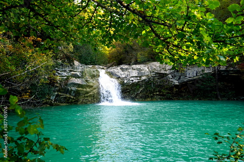 Waterfall in the woods flowing towards a turquoise lake