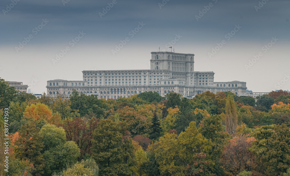 Palace of the Parliament building in Bucharest - top view with a cloudy sky above and autumn fall trees in foreground