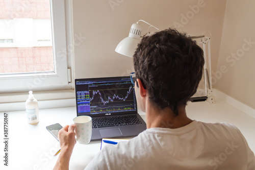 businessman working from home, watching on his laptop the stocks of his company while having a coffee