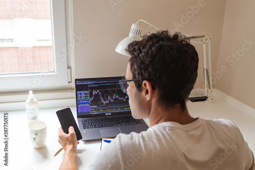 businessman working from home, watching on his laptop the stocks of his company and answering the mobile phone