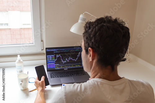 businessman working from home, watching on his laptop the stocks of his company and answering the mobile phone