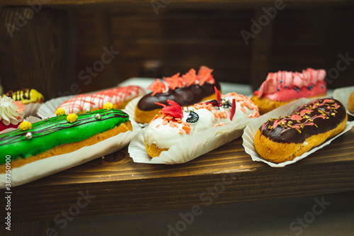 Amazing fresh colorful home-made eclairs close up. Delicious sweets. Tasty french multicolored eclairs with icing, cream, fresh berries decor elements. Original french multicolored eclairs.