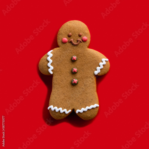 Christmas cookie. Festive pastry. Homemade biscuit. Brown happy gingerbread man decorated with white icing smiling isolated on red background.