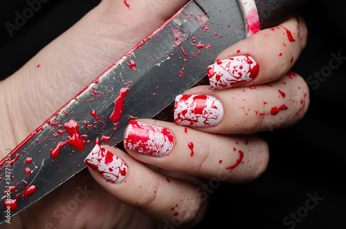 Bloody manicure for Halloween with drops of blood and a fingerprint with a knife on a black background