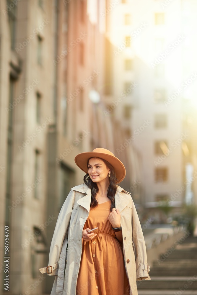 Young beautiful and stylish caucasian woman wearing long romantic dress and hat looking aside and thinking about something while standing on the city street
