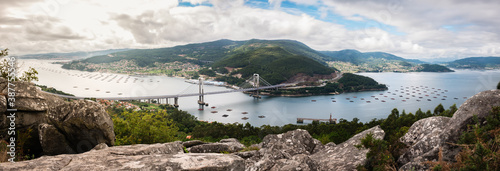Panorama view of the Ria de Vigo estuary from Redondela on a cloudy Summer afternoon, with the recently extended Rande bridge on the center and the Atlantic Ocean on the left. Long exposure.