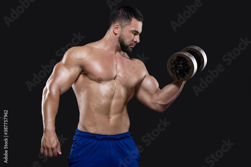 A handsome beefy man is focused on performing the exercise lifting a dumbbell with one hand isolated on black background