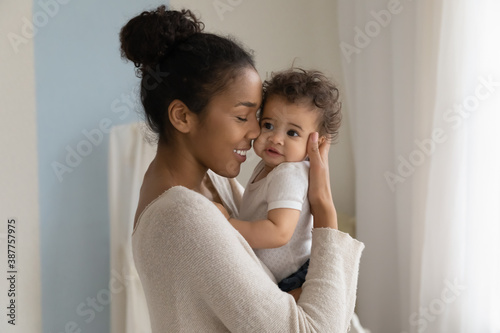 Fotografia Happy young African American mom hold in hands hug cute little ethnic baby toddler show love care