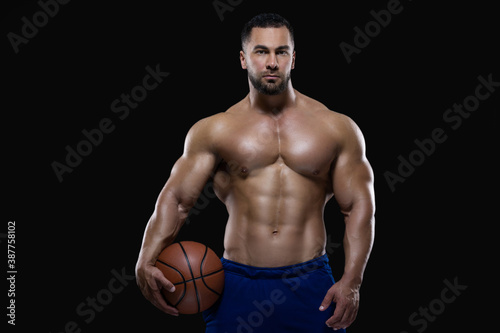 Front view portrait of an attractive sportsman holding a basketball with one hand isolated on black background © satyrenko