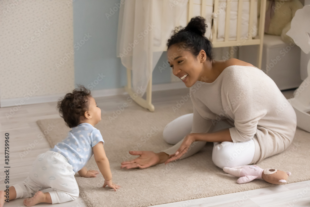 Smiling african American young mom sit on floor in children room play with small biracial toddler baby. Happy loving ethnic mother have fun learn walking crawling at home. Childcare concept.