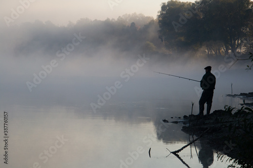 Morning fog at dawn. Autumn landscape, river bank, trees, in the distance a fisherman with a fishing rod