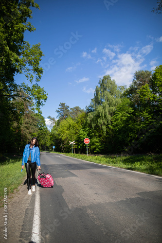 The teenager returns on foot along the asphalt road among lush greenery - wonderful trees and shrubs.