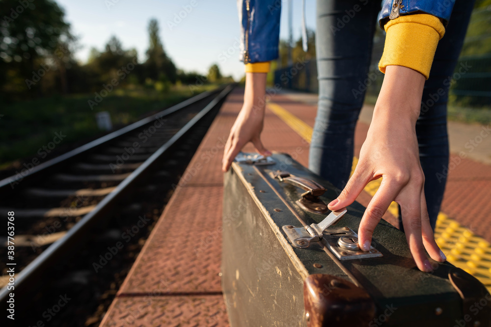 A girl fastens the zipper on an old travel suitcase on a train platform one summer afternoon during a planned train trip.