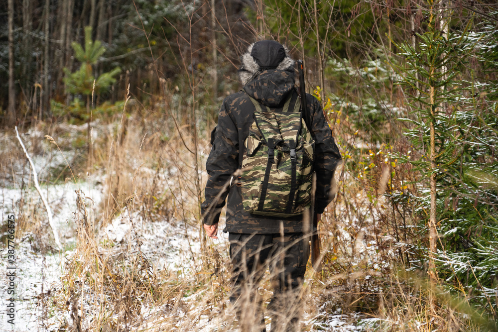 Hunter with a gun and a backpack in the winter forest