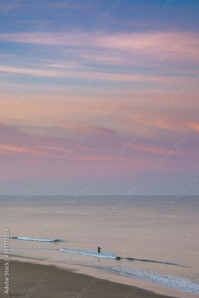 lone fisherman in the surf at a wild and empty beach during a beautiful sunrise