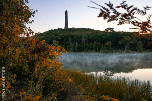 Tall obelisk monument on a mountain framed in fall foliage at sunrise. High Point State Park, New Jersey