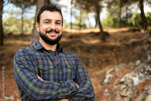 Man with beard and plaid shirt of aesthetic lumberjack crosses his arms in the middle of nature in portrait looking at camera photo