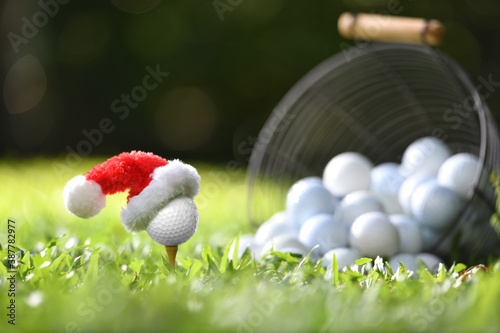 Festive-looking golf ball on tee with Santa Claus' hat on top for holiday season on golf course background..