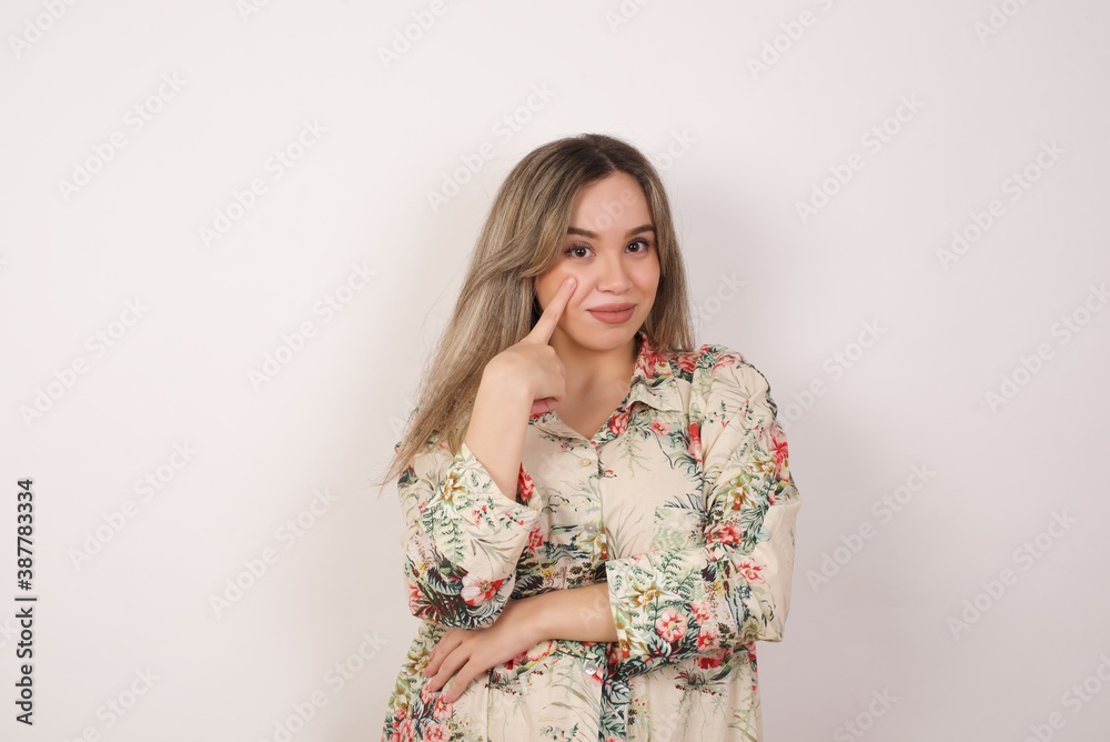 Young beautiful woman standing against yellow background, looking, observing, keeping an eye on an object in front, or watching out for something.