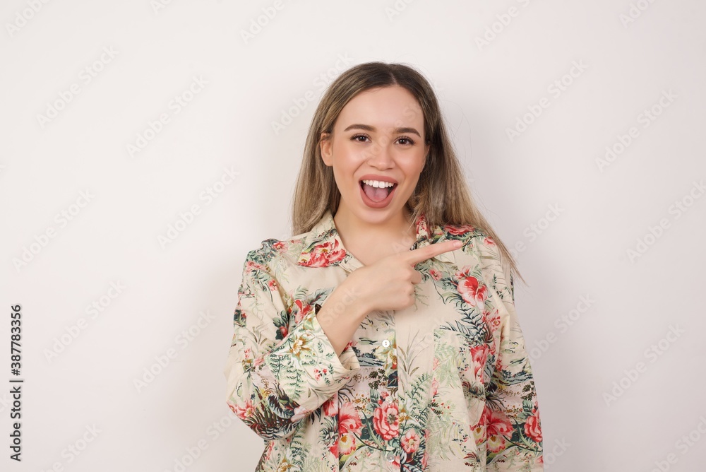Look over there! Beautiful woman wearing colorful shirt over yellow background pointing away and smiling to you while standing against grey background. Look over there! Beautiful woman wearing colorful shirt over yellow background pointing away and smiling to you while standing against grey background.