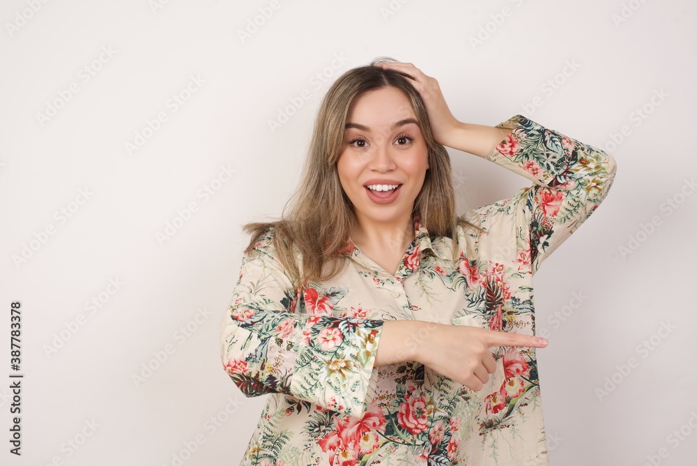 Positive glad female says: wow how exciting it is, has amazed expression, indicates something. Joyful pretty young woman demonstrates something. One hand on her head and pointing with other hand. Positive glad female says: wow how exciting it is, has amazed expression, indicates something. Joyful pretty young woman demonstrates something. One hand on her head and pointing with other hand.