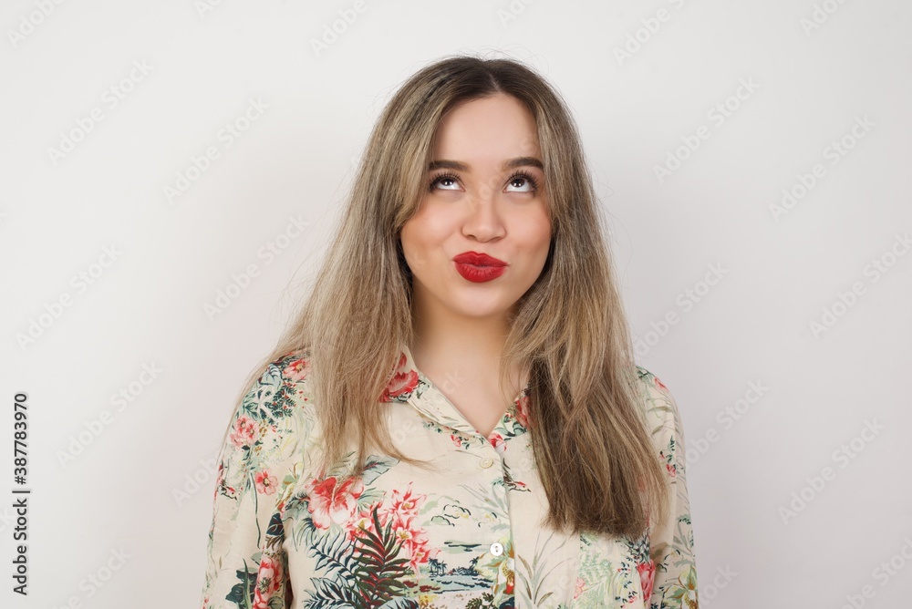 Gloomy, wondering young woman looking up with lips together, being upset thinking about something important, keeps hands down. Gloomy, wondering young woman looking up with lips together, being upset thinking about something important, keeps hands down.