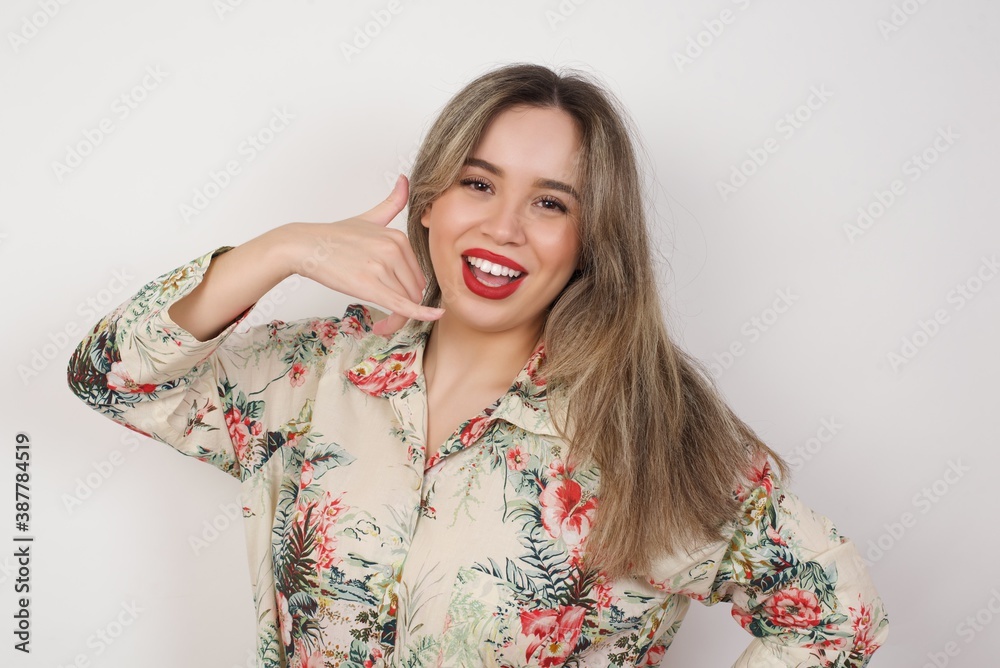 Attractive young female standing against yellow background in casual clothes, makes phone call gesture, imitates telephone conversation. Call me! Attractive young female standing against yellow background in casual clothes, makes phone call gesture, imitates telephone conversation. Call me!