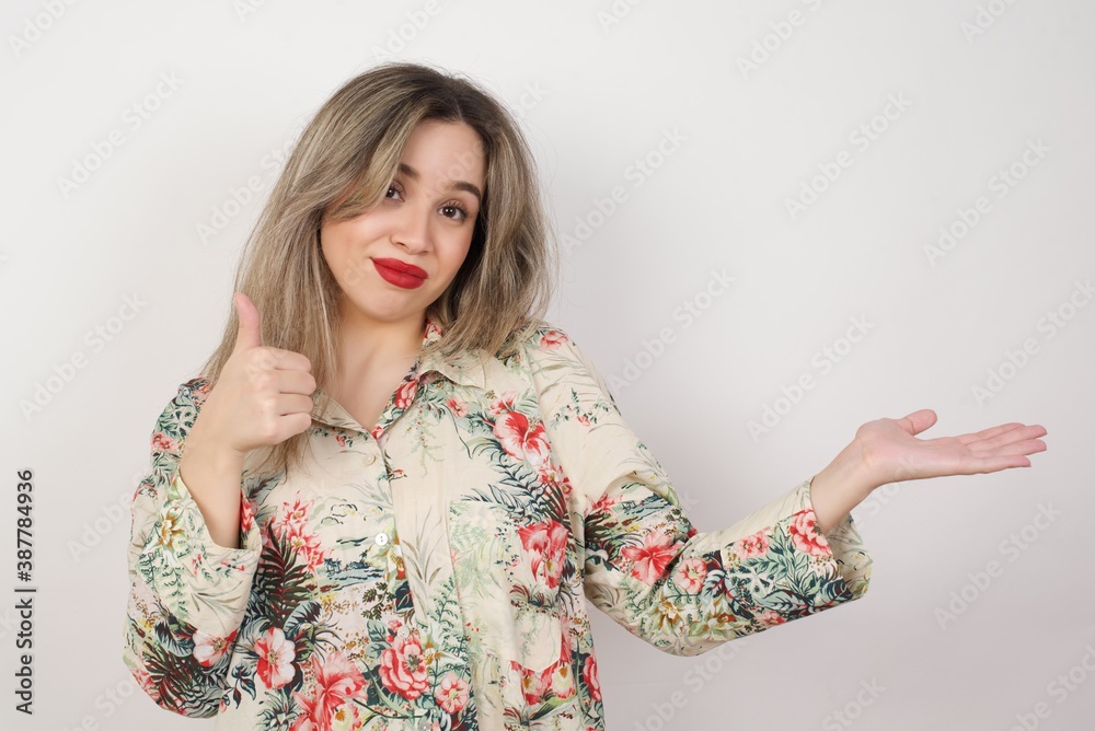 Young happy cheerful woman showing thumb up and pointing with the other hand while standing outdoors. Good Job. Wearing casual clothes. Young happy cheerful woman showing thumb up and pointing with the other hand while standing outdoors. Good Job. Wearing casual clothes.