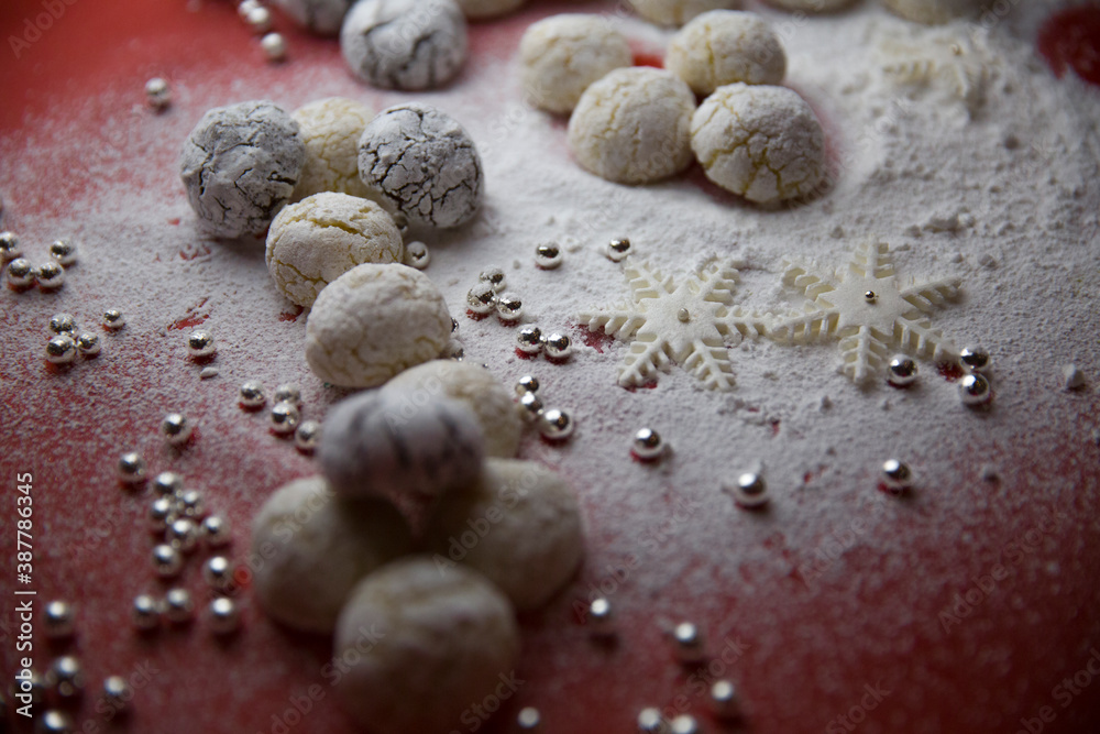 Handmade cookies, decorative snowflakes, decorative pearls and powdered sugar on the table. White on red.