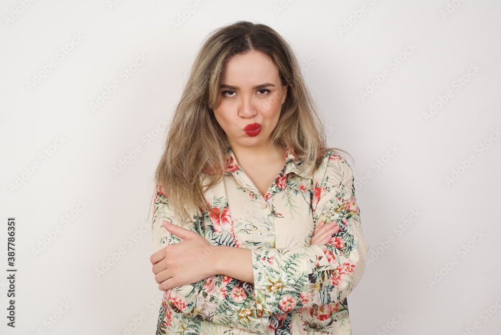 Picture of angry young Caucasian young blonde woman standing against white background crossing arms standing isolated over background. Looking at camera. Picture of angry young Caucasian young blonde woman standing against white background crossing arms standing isolated over background. Looking at camera.