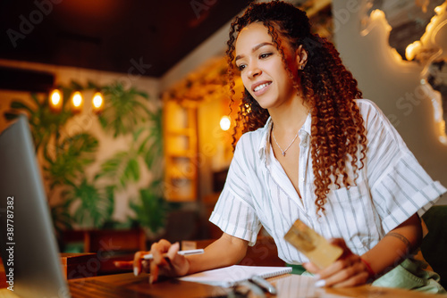 African American woman with credit card and laptop computer doing online shopping sitting at cafe or restaurant. Online shopping, e-commerce, internet banking, spending money.